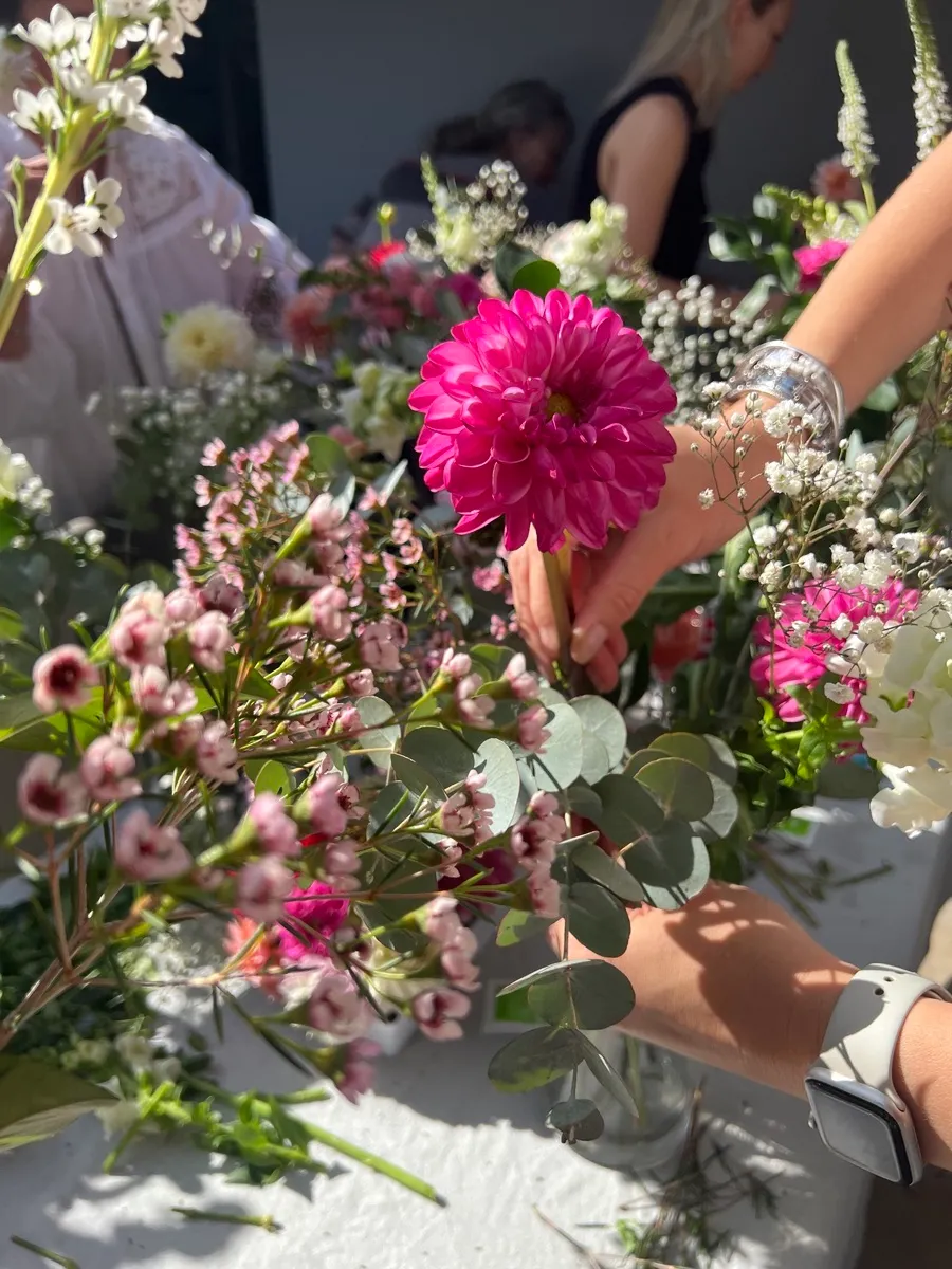 Hands arranging a bright pink dahlia and seasonal blooms at a Mamma's Plants workshop