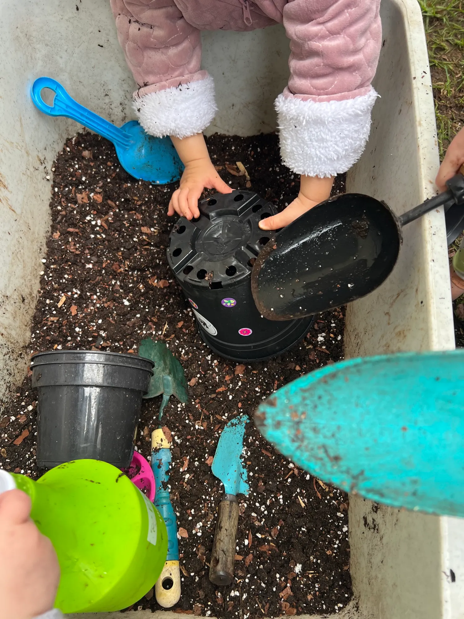 Little hands scooping soil around a sticker-decorated pot in a soil tray
