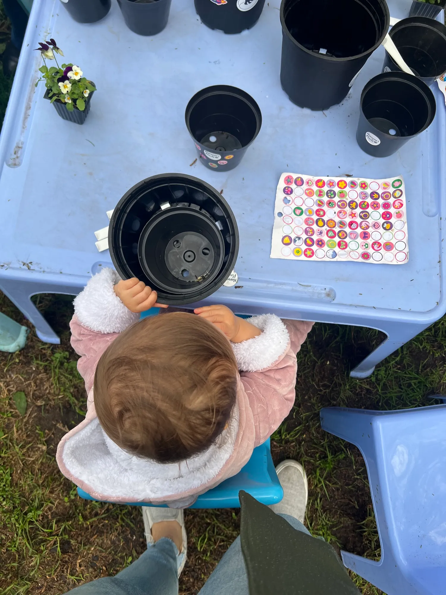 A toddler at a low table with plant pots and a sheet of stickers to decorate them